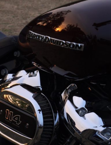Close-up of a black motorcycle engine with a shiny chrome finish and reflection of trees.