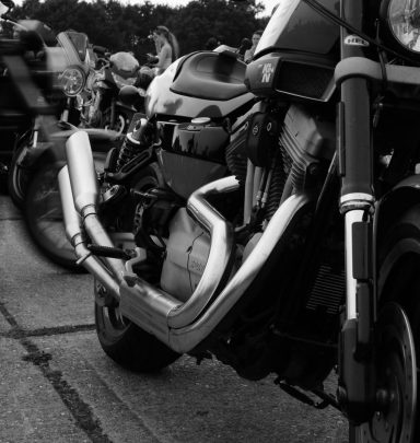 Close-up of a motorcycle exhaust in black and white, with other bikes in the background.